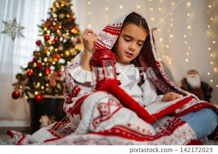 Young girl reading book under blanket holding lantern Young girl reading book under blanket holding lantern 142172023