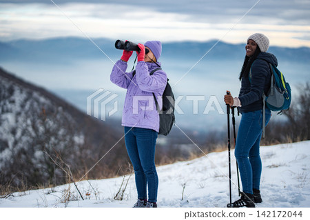 Friends hiking in snow with binoculars exploring winter mountains Friends hiking in snow with binoculars exploring winter mountains 142172044