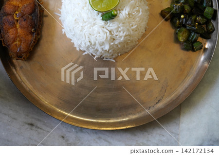 Traditional Bengali meal served on a brass plate with rice fish fry and okra fry Traditional Bengali meal served on a brass plate with rice fish fry and okra fry 142172134