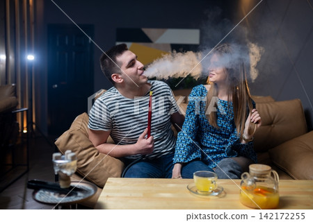 Man blowing smoke towards a woman on a lounge sofa Man blowing smoke towards a woman on a lounge sofa 142172255