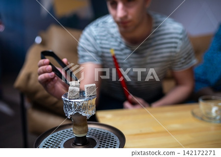 Man adjusting burning charcoal on top of a hookah bowl Man adjusting burning charcoal on top of a hookah bowl 142172271