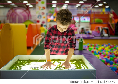 Boy creating patterns with green sand on a light table Boy creating patterns with green sand on a light table 142172279