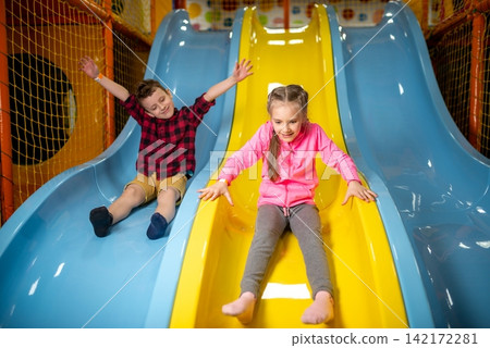 Children sliding down adjacent playground slides together Children sliding down adjacent playground slides together 142172281