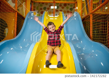 Happy boy sliding down a yellow slide indoors Happy boy sliding down a yellow slide indoors 142172282