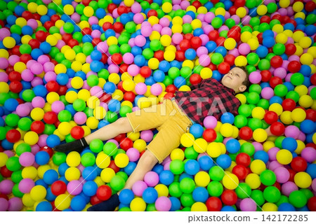 Boy lying down in a colorful ball pit Boy lying down in a colorful ball pit 142172285
