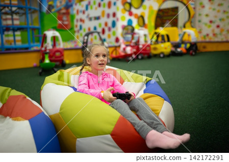 Girl holding a controller while sitting in a bean bag Girl holding a controller while sitting in a bean bag 142172291
