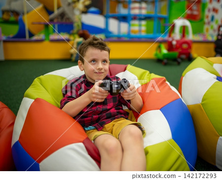 Close portrait of a boy with a controller sitting in a bean bag Close portrait of a boy with a controller sitting in a bean bag 142172293