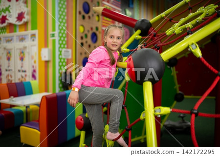 Girl climbing on a colorful rope playground structure Girl climbing on a colorful rope playground structure 142172295