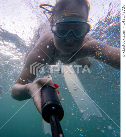 Swimming adventure selfie of young woman diving underwater with action camera wearing goggles and flippers Swimming adventure selfie of young woman diving underwater with action camera wearing goggles and flippers 142172726