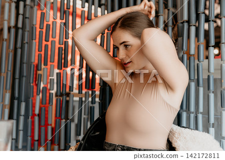 Woman portrait hairstyle young lady fixing her bun in a modern interior setting with a decorative cylinder wall backdrop Woman portrait hairstyle young lady fixing her bun in a modern interior setting with a decorative cylinder wall backdrop 142172811