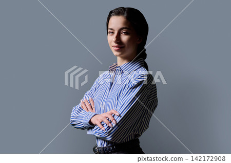 Confident young female student standing with crossed arms looking at camera against studio background Confident young female student standing with crossed arms looking at camera against studio background 142172908