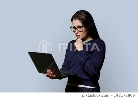 Mature woman in glasses holding and typing on laptop studio portrait 142172909