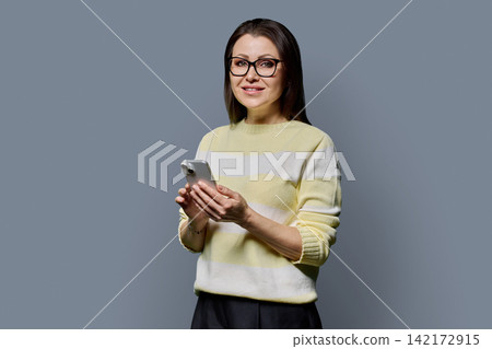 Smiling 40s mature woman using smartphone portrait on grey background Smiling 40s mature woman using smartphone portrait on grey background 142172915