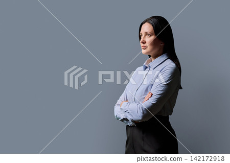 Confident businesswoman standing with arms crossed on gray studio background 142172918