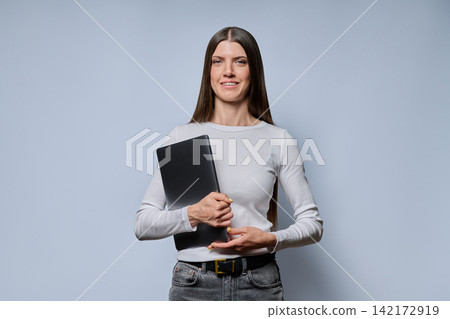 Portrait of happy smiling young woman holding laptop computer on grey background 142172919