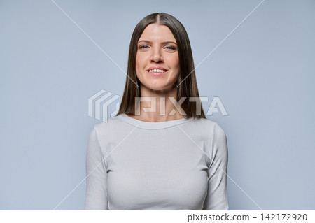 Portrait of a confident young woman with long dark hair smiling on grey background Portrait of a confident young woman with long dark hair smiling on grey background 142172920