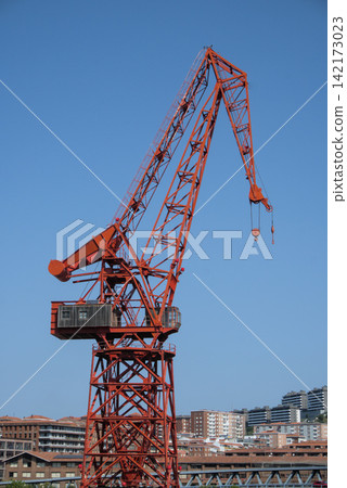 A preserved red harbour crane rising above city rooftops under a clear blue sky A preserved red harbour crane rising above city rooftops under a clear blue sky 142173023