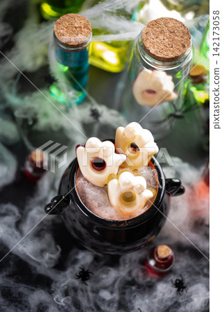 Spooky Halloween cauldron filled with ghost shaped candy and surrounded by potion bottles and cobwebs Spooky Halloween cauldron filled with ghost shaped candy and surrounded by potion bottles and cobwebs 142173058