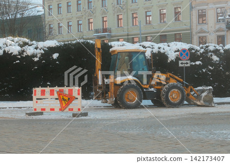 Yellow tractor parked on a snowy city street during winter season Yellow tractor parked on a snowy city street during winter season 142173407