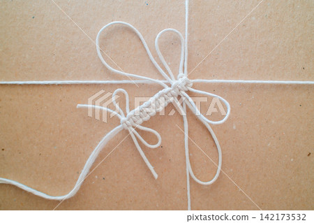 Crafting white macrame dragonfly knot on brown surface 142173532