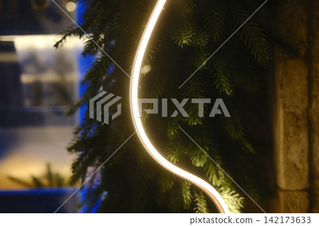 Bright neon light glowing beside green spruce branches at night time Bright neon light glowing beside green spruce branches at night time 142173633