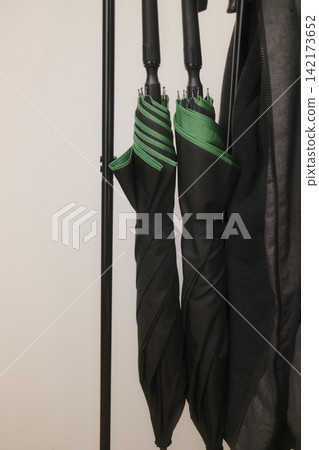 Closed black umbrellas with green details hanging on a metal coat rack Closed black umbrellas with green details hanging on a metal coat rack 142173652