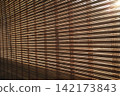 Sunlight streams through natural bamboo blinds, casting warm 142173843