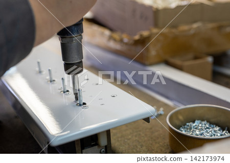 Hand using power drill to fasten screws into white metal panel in workshop Hand using power drill to fasten screws into white metal panel in workshop 142173974