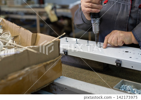 Worker assembling white metal panel with power drill in workshop Worker assembling white metal panel with power drill in workshop 142173975