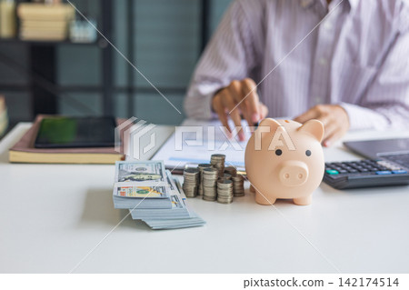 Saving money with piggy bank and stack of coins on a table in a home office. Saving money with piggy bank and stack of coins on a table in a home office. 142174514