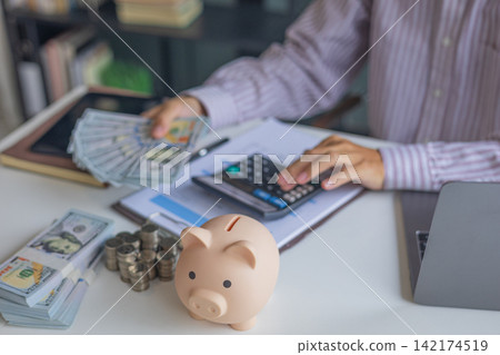 Saving money with piggy bank and stack of coins on a table in a home office. Saving money with piggy bank and stack of coins on a table in a home office. 142174519
