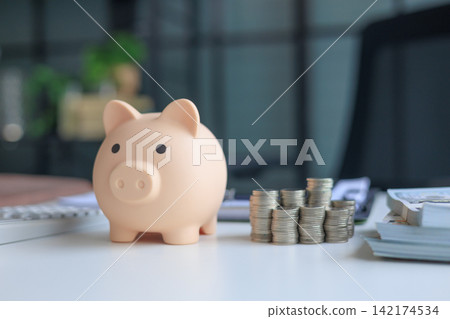 Office table with piggy bank, coin stacks, and paper banknotes. Concept for money saving and management. Office table with piggy bank, coin stacks, and paper banknotes. Concept for money saving and management. 142174534