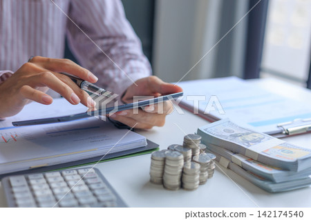 Accountant using tablet analyzing financial reports on tablet with calculator, cash and coins on desk. Accountant using tablet analyzing financial reports on tablet with calculator, cash and coins on desk. 142174540