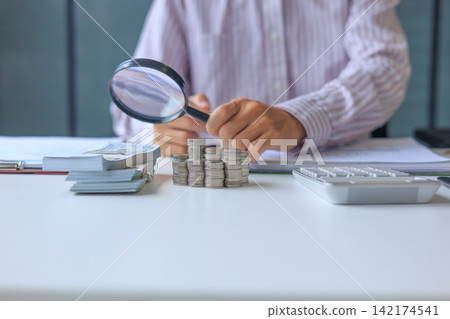 Financial Auditor Reviewing Business Accounting Documents and Money Assets with Magnifying Glass. Financial Auditor Reviewing Business Accounting Documents and Money Assets with Magnifying Glass. 142174541