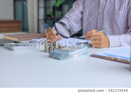 Financial Auditor Reviewing Business Accounting Documents and Money Assets with Magnifying Glass. Financial Auditor Reviewing Business Accounting Documents and Money Assets with Magnifying Glass. 142174544