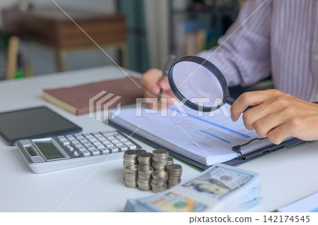 A person using magnifying glass to conduct a financial audit and bookkeeping review. financial analysis and forensic accounting to prevents leaks and invoicing errors. A person using magnifying glass to conduct a financial audit and bookkeeping review. financial analysis and forensic accounting to prevents leaks and invoicing errors. 142174545