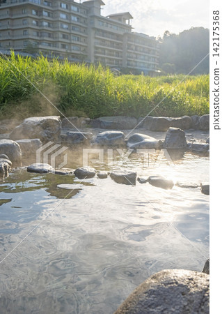 A riverside open-air bath in Misasa Onsen, surrounded by lush greenery. A riverside open-air bath in Misasa Onsen, surrounded by lush greenery. 142175368