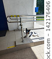 A black and white dog is lying on a tiled ramp next to a building entrance. The ramp has stainless steel handrails with yellow tape markings 142176406