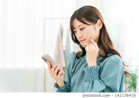 A woman looking at her smartphone, confused, worried, confused A woman looking at her smartphone, confused, worried, confused 142176410