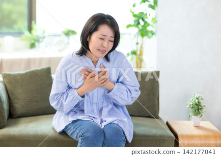 A middle-aged woman clutches her chest, feeling unwell. A middle-aged woman clutches her chest, feeling unwell. 142177041
