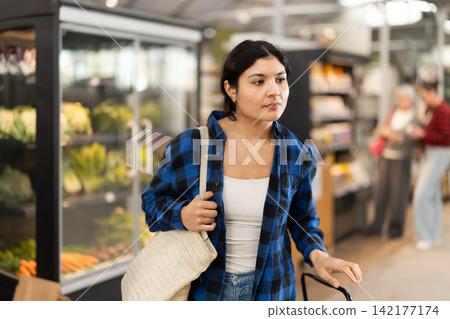 Woman in supermarket sales area looks into distance and searches for necessary goods Woman in supermarket sales area looks into distance and searches for necessary goods 142177174