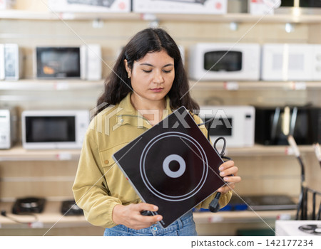Young woman choosing portable electric cooktop at household appliances store Young woman choosing portable electric cooktop at household appliances store 142177234
