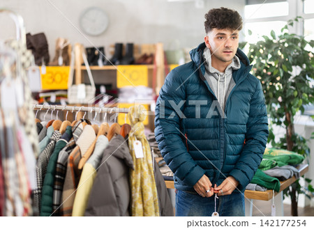 Young man tries on down jacket in clothing store Young man tries on down jacket in clothing store 142177254