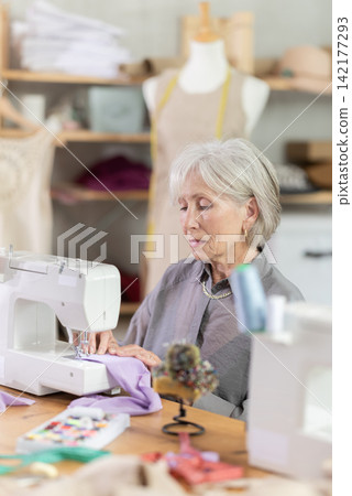 woman dressmaker sews on a machine in a workshop woman dressmaker sews on a machine in a workshop 142177293