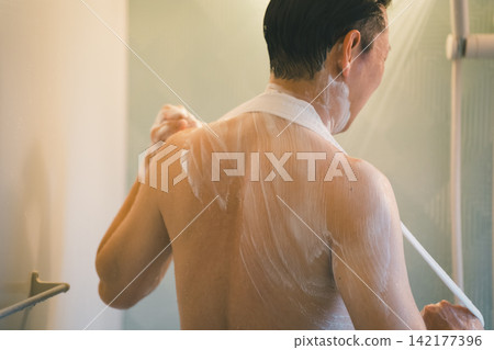 A man's bath time: thoroughly washing his back with a body towel. A man's bath time: thoroughly washing his back with a body towel. 142177396