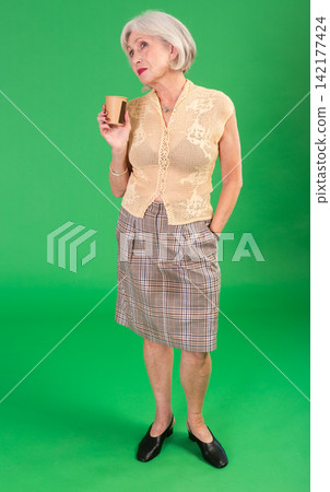 Senior woman in beige suit and coffee break on green screen background. Senior woman in beige suit and coffee break on green screen background. 142177424