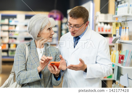 Old female customer asking middle-aged chemist about product reflected on her phone Old female customer asking middle-aged chemist about product reflected on her phone 142177428
