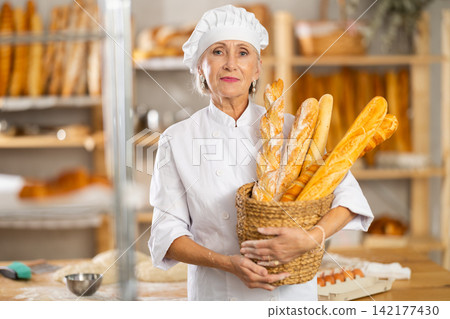 Positive elderly woman bakery employee offering bread and different baguettes for sale Positive elderly woman bakery employee offering bread and different baguettes for sale 142177430