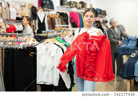Young girl choosing red blouse in clothing store Young girl choosing red blouse in clothing store 142177438