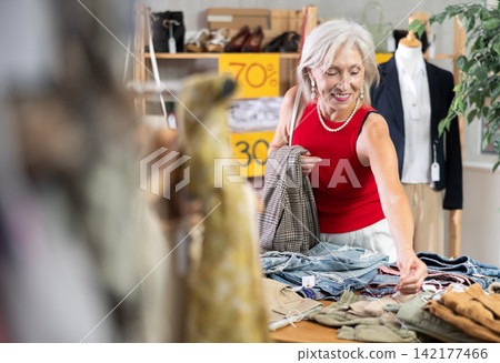 Elderly woman choosing trousers in clothing store Elderly woman choosing trousers in clothing store 142177466